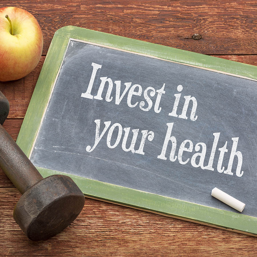 Invest in your health -  slate blackboard sign against weathered red painted barn wood with a dumbbell, apple and tape measure